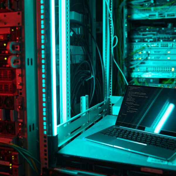 Background image of opened laptop by server cabinet in data center lit by blue light, copy space