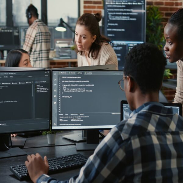 Mixed team of artificial intelligence cloud programers talking about programming in front of multiple screens compiling code. Programmers doing teamwork looking at machine learning algorithms.